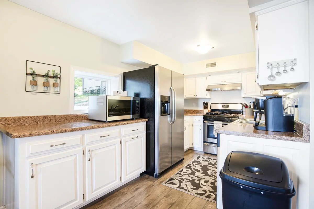 A welcoming kitchen scene with granite countertops, stainless steel appliances, decorative wall art, and a patterned kitchen rug. The layout invites group cooking and casual conversation, underscoring the kitchen as a social hub.