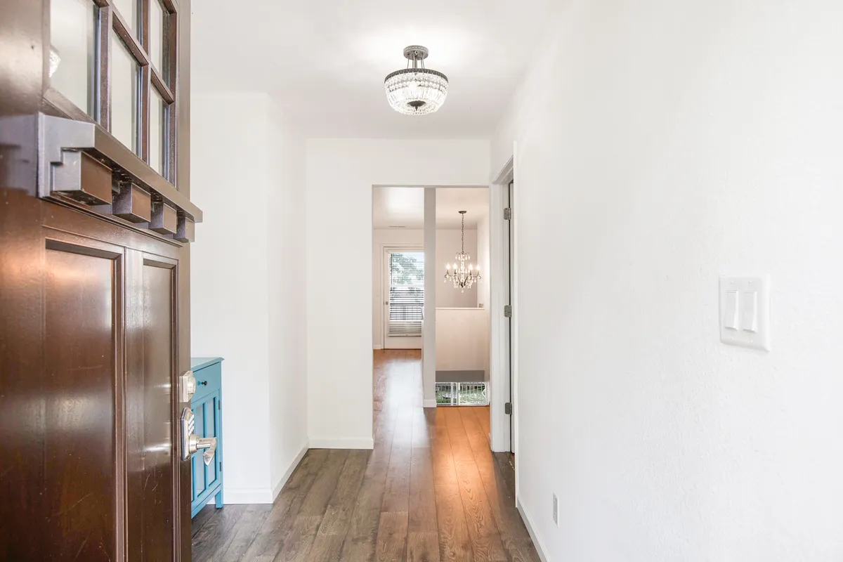 A bright and inviting entryway with a stylish blue console table, chandelier, and a welcoming entrance door. The space is thoughtfully decorated, giving a sense of arrival and hospitality.